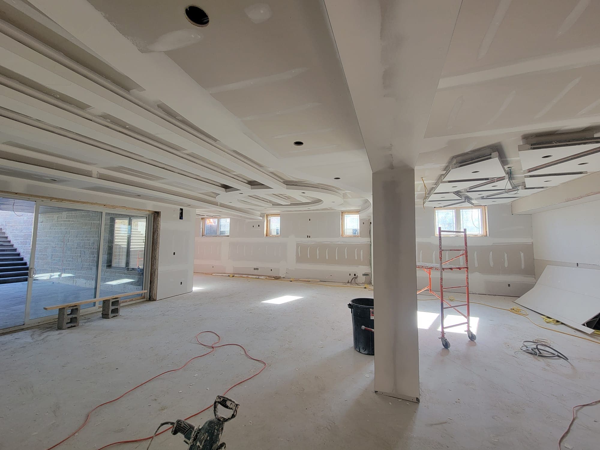 Large room under construction featuring elaborate drywall ceiling designs, a support column, and scaffolding.