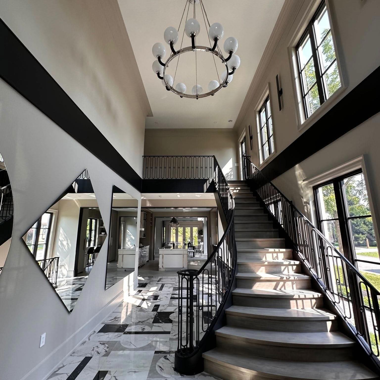 Luxurious foyer with a curved staircase, marble floors, diamond mirrors, and a modern chandelier.